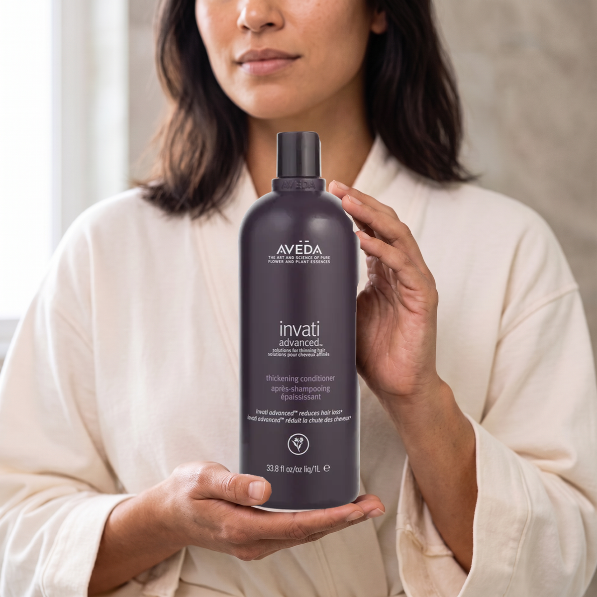 Adult woman holding Aveda Invati Advanced Thickening Conditioner, 1 L; styled AI lifestyle scene