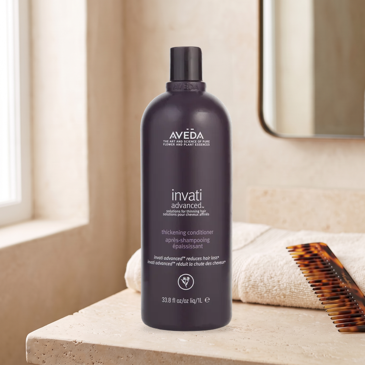 Aveda Invati Advanced conditioner bottle on a stone bathroom vanity with towel and comb; styled AI scene